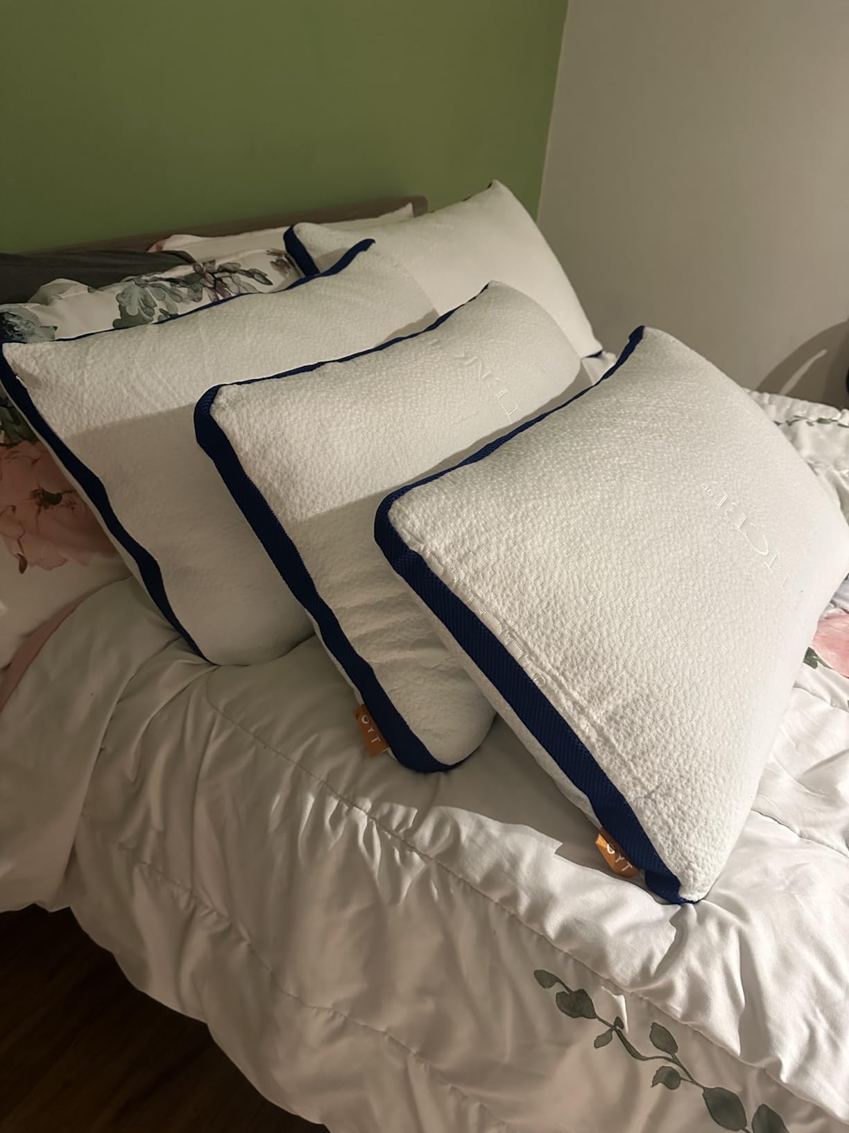 A bed featuring three OYT Cooling Bed Pillows, set against a green wall, demonstrating their cozy look in use.