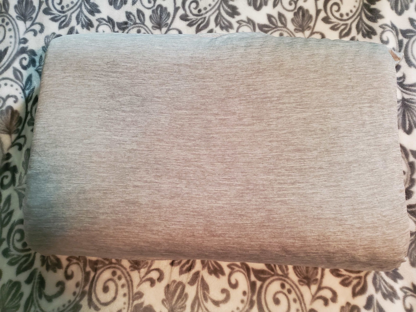 A gray blanket draped over a bed, featuring a white pillow, showcasing the LUXEAR cooling pillow in use for a product review.