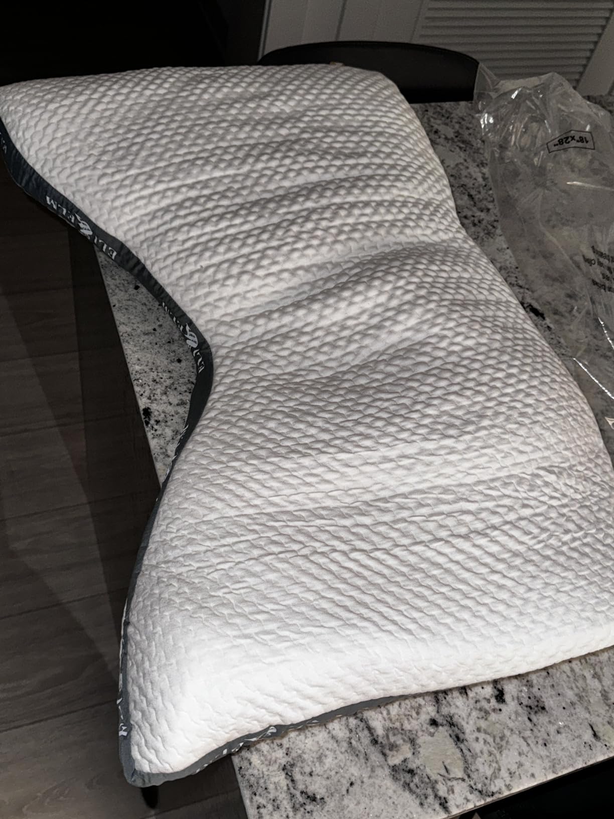 The Ultimate Side Sleeper Pillow rests on a counter beside a glass of water, demonstrating its use for a product review.