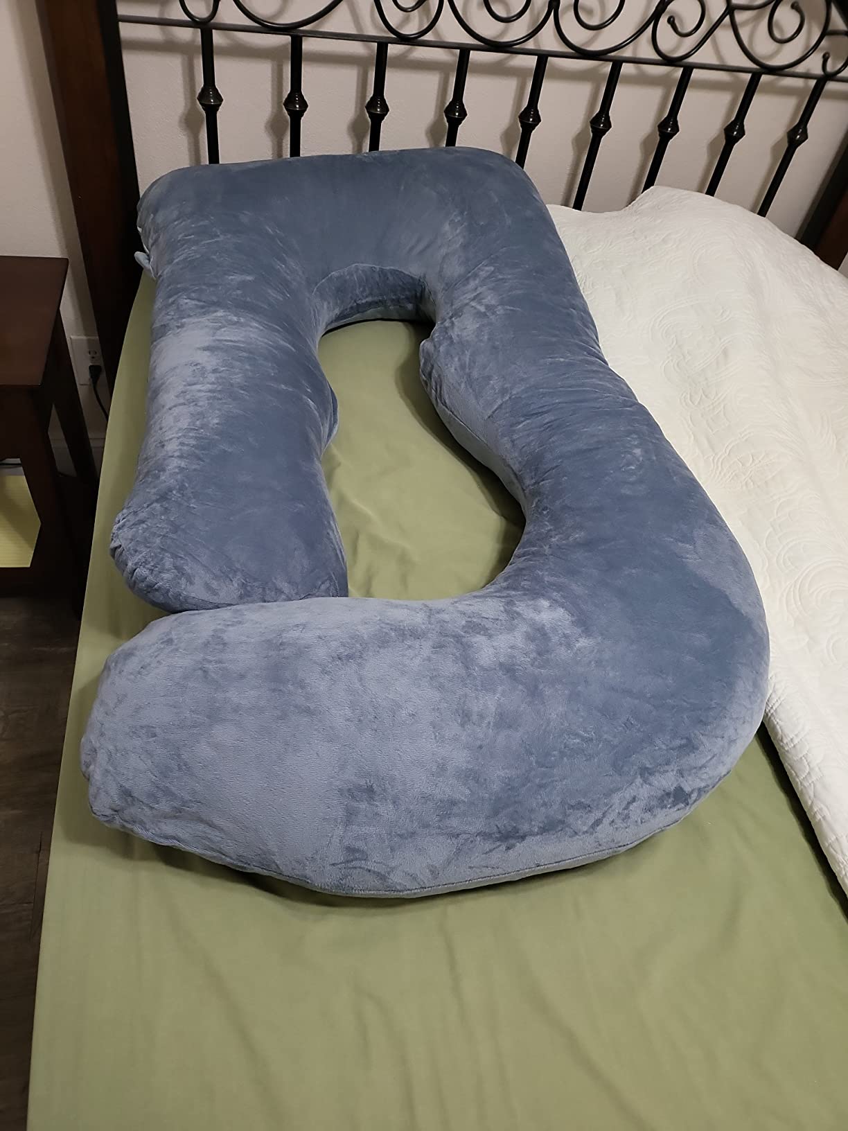 A blue Chilling Home Pregnancy Pillow is placed on a bed with a green sheet, highlighting its cozy and inviting appearance.