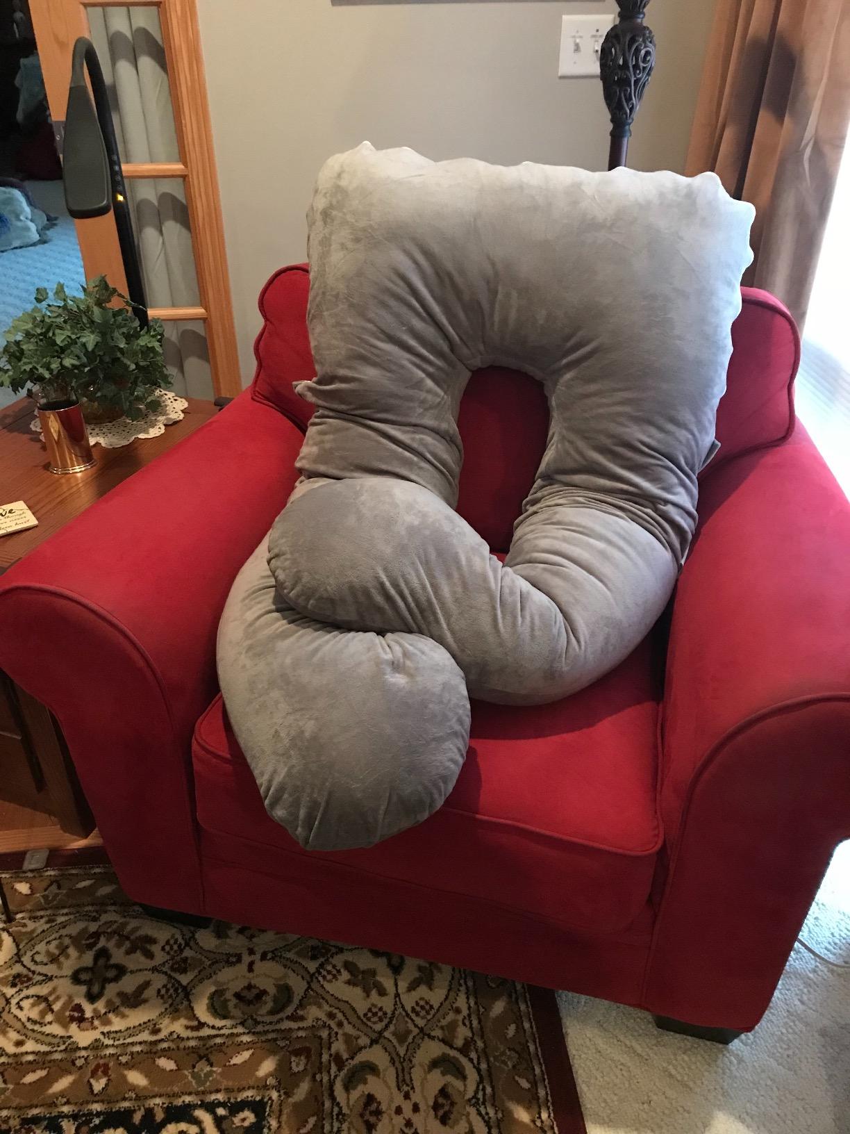 A large Meiz Pregnancy Pillow rests comfortably on a red chair, showcasing its soft and supportive design. In product review setting.