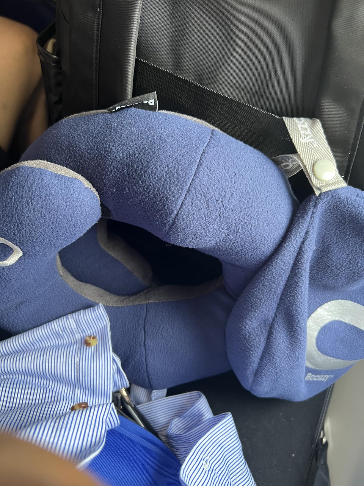 A blue BCOZZY Neck Pillow for Travel alongside a blue bag on an airplane seat, demonstrating travel essentials in use.