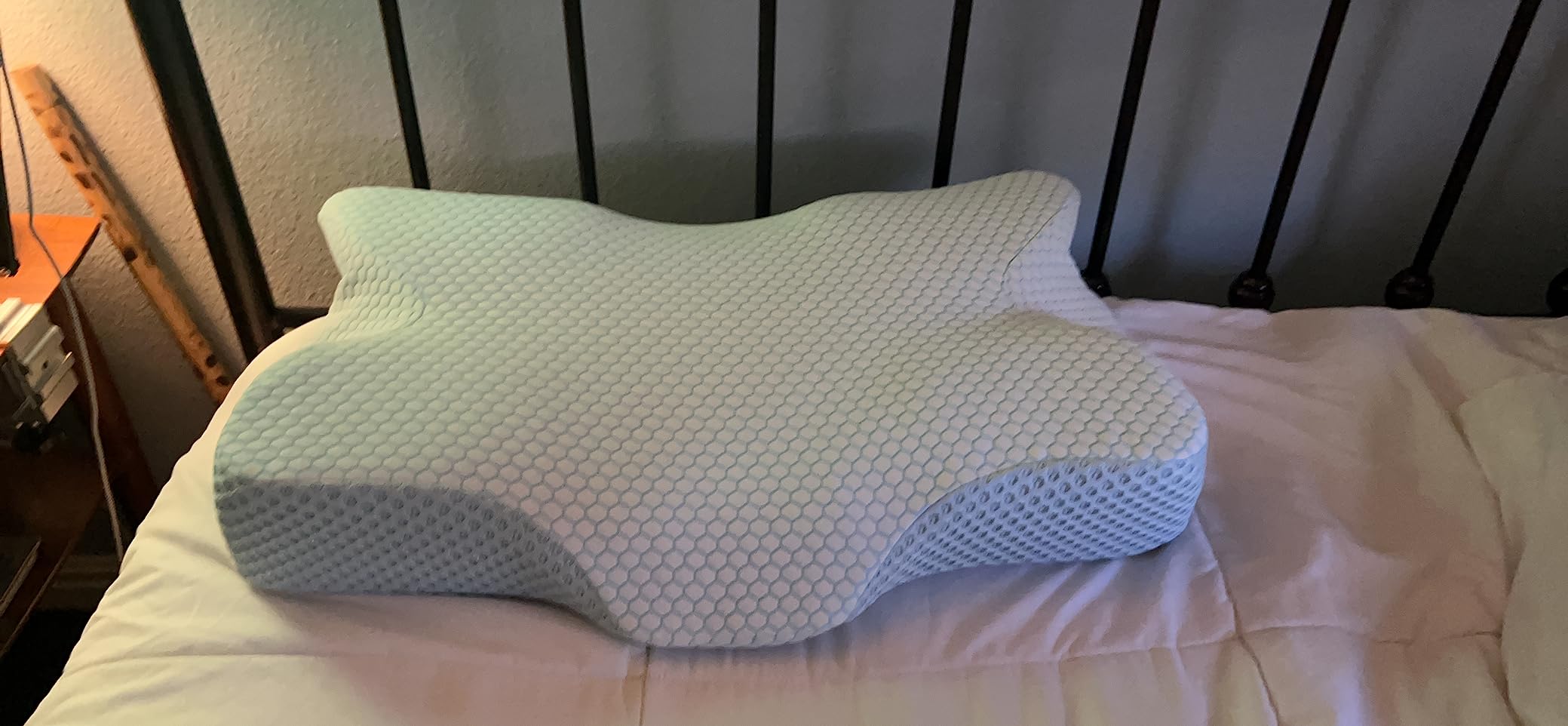 A white-covered bed with an Anvo Cervical Pillow resting on it, showcasing its comfort and design for a product review.